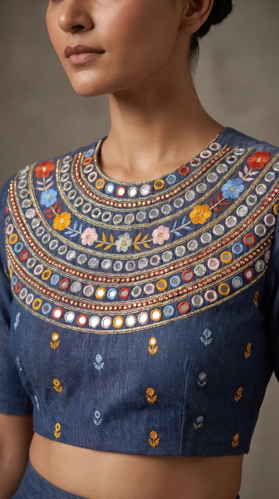 Close-up of multicoloured floral hand embroidery and mirror work on blue denim blouse