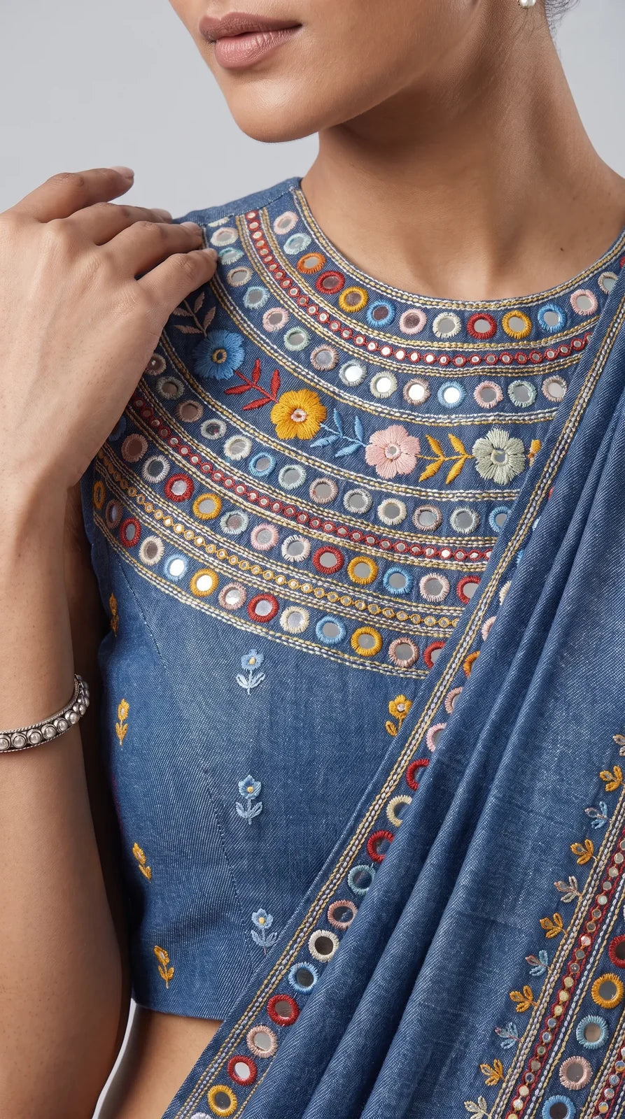 Close-up of floral hand embroidery and mirror work on blue denim saree blouse and border